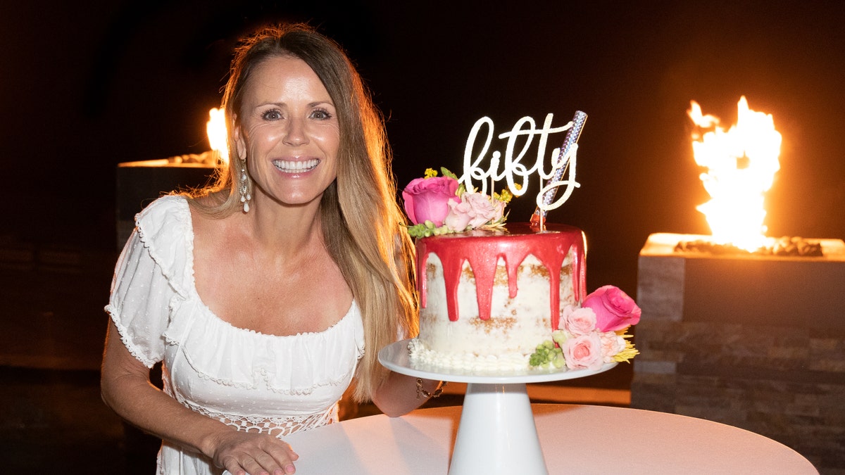 Trista Sutter with a white dress on celebrates her 50th birthday with a white and pink cake