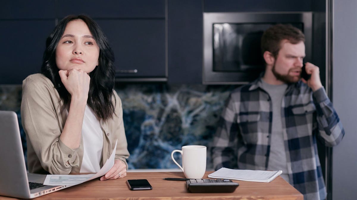 Men and woman standing in the kitchen, upset at each other.