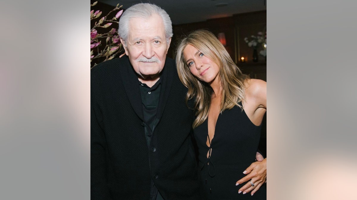 Jennifer Aniston in a black outfit leans her head in towards father John, also in black