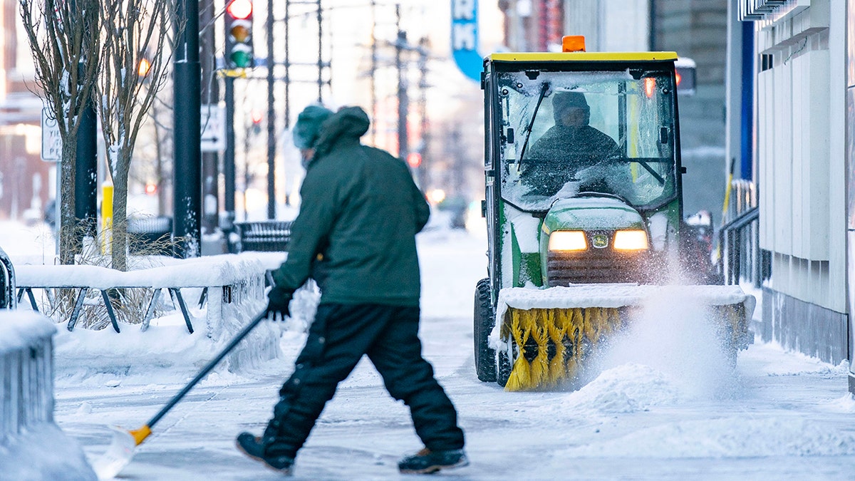 Man shovels snow while another uses power sweeper in downtown Minneapolis on Thursday, Dec. 22, 2022