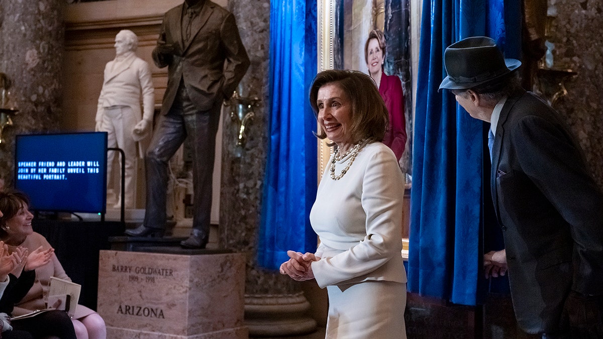 Pelosi standing with her hands clasped