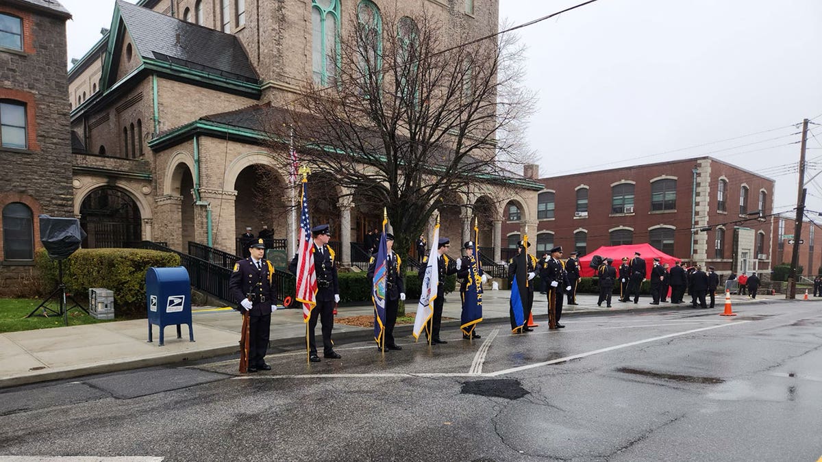 Four policemen hold flags to their sides outside of a church