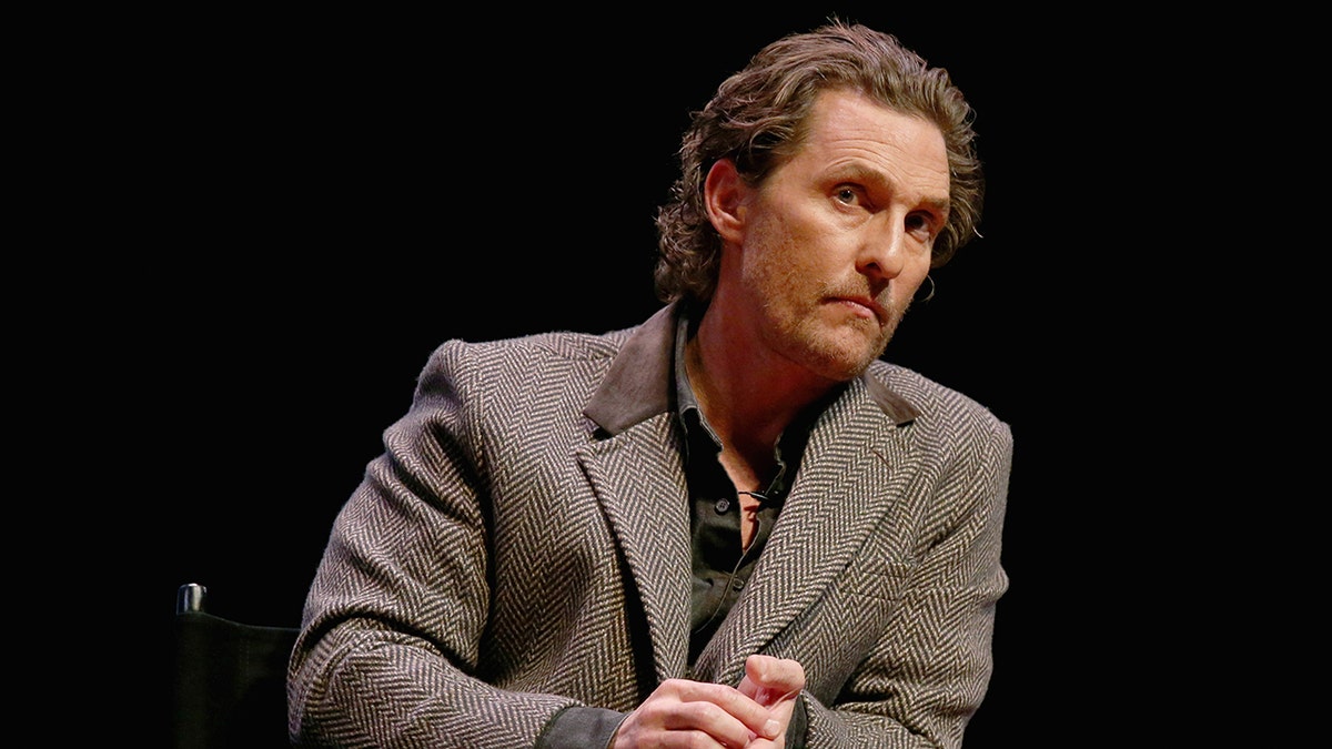 Matthew McConaughey in a brown chevron suit looks off in the distance and clasps his hands