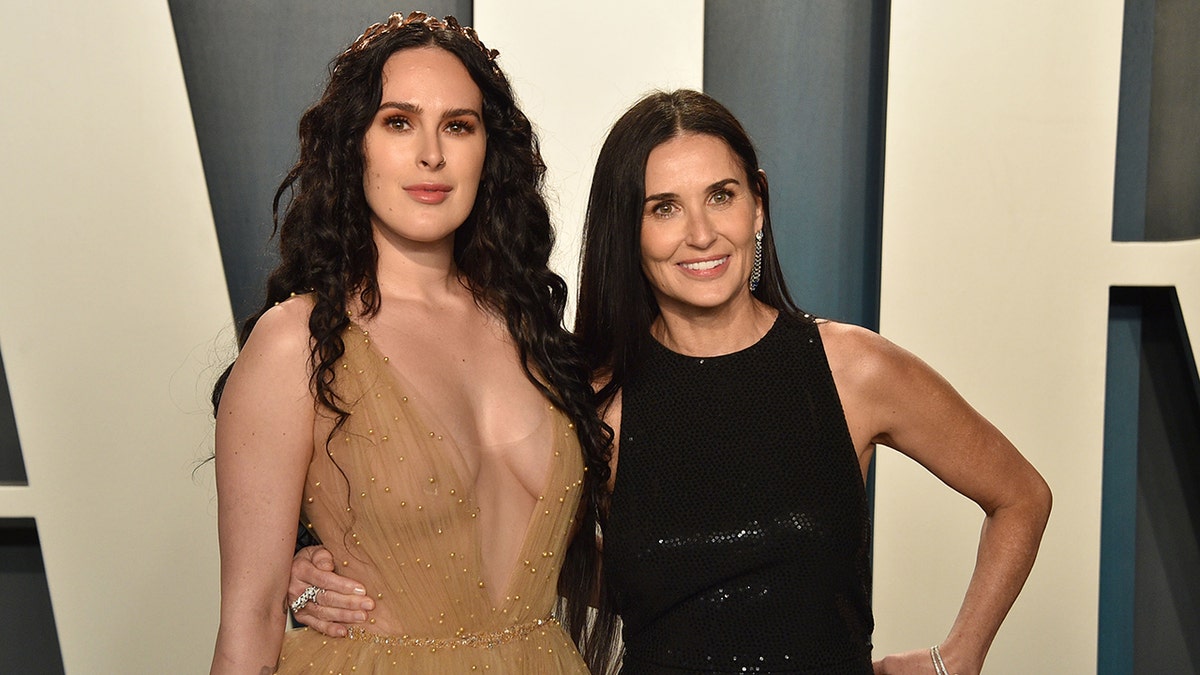 Rumer Willis in a tan deep V dress alongside Demi Moore in a black dress on the Vanity Fair Oscar's red carpet