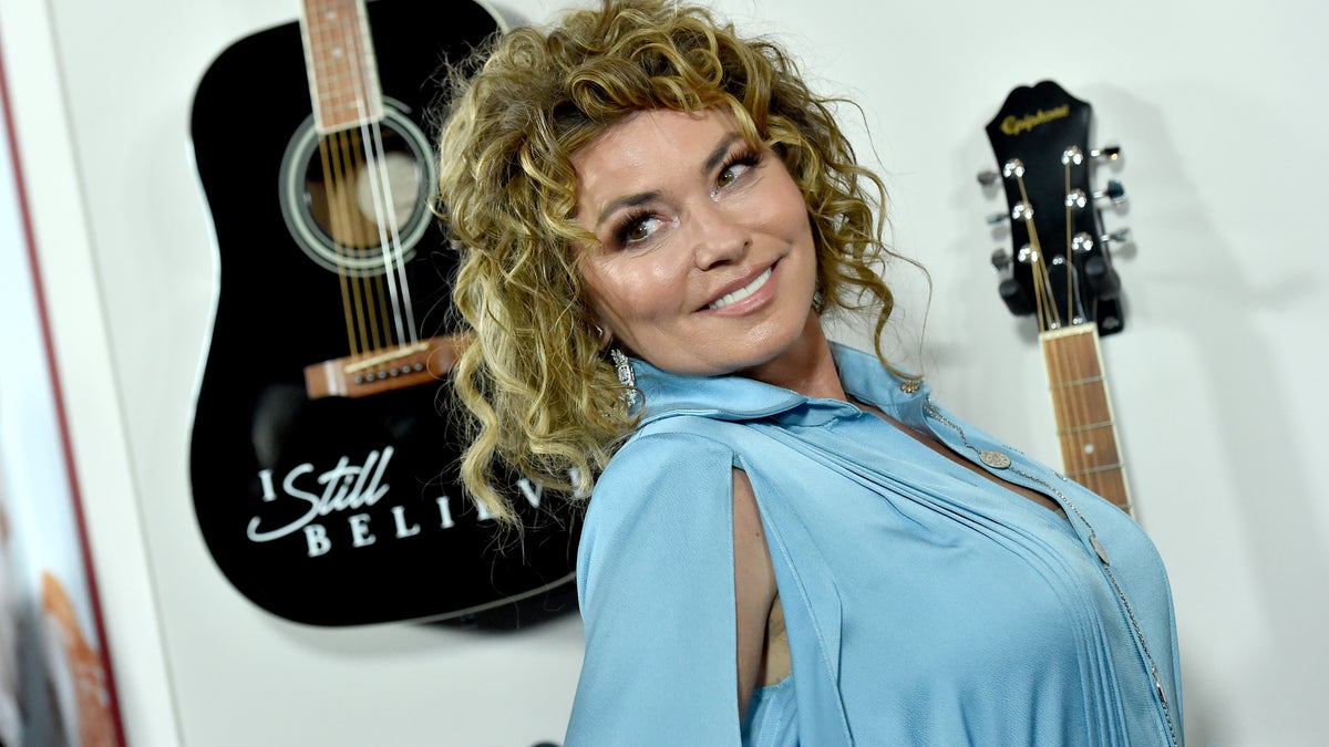 Shania Twain smiles to the right in a blue gown and curly hair updo