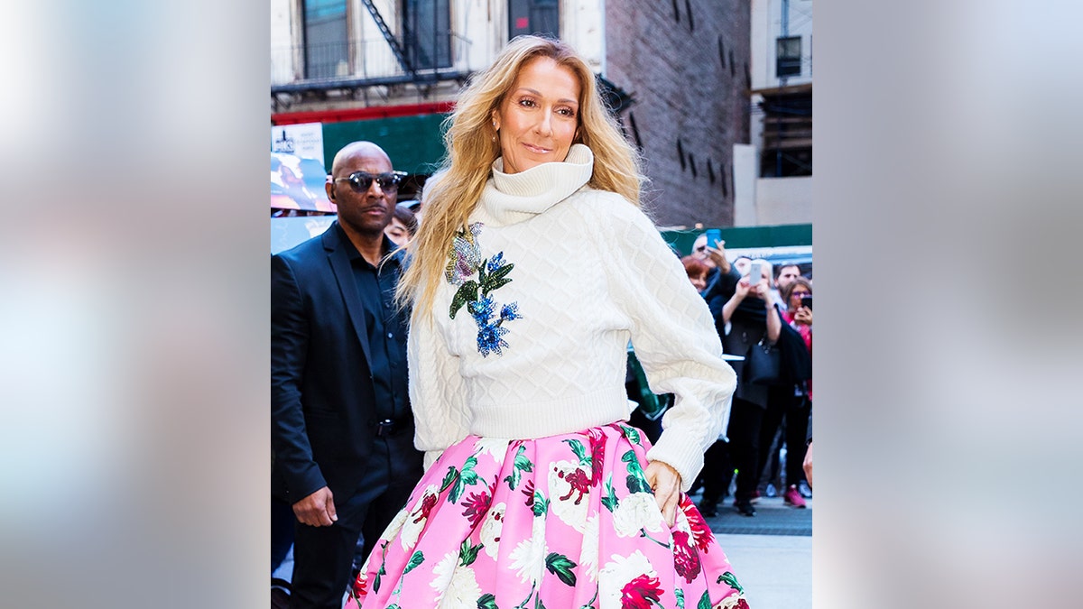 Celine Dion in a white sweater and floral print bubblegum pink skirt