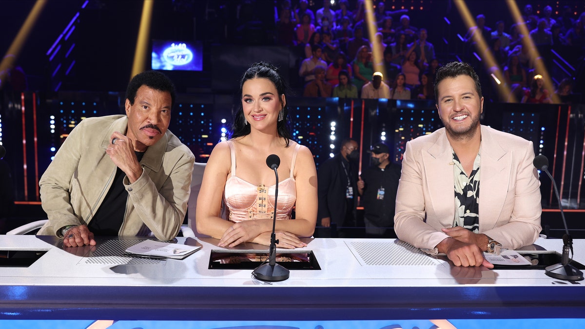 Lionel Richie in a tan jacket, Katy Perry in satin dress, and Luke Bryan in a light pink suit sit at the judges table on "American Idol'
