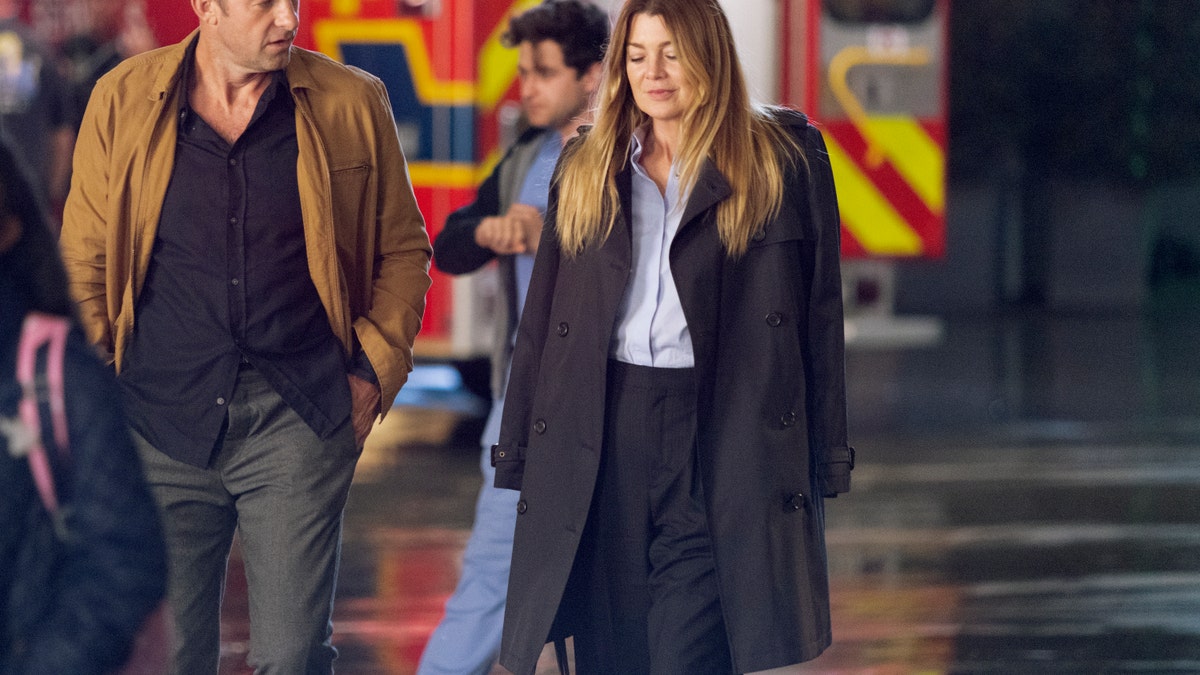 Nick Marsh (Scott Speedman) in a brown/orange suit walks alongside Meredith Grey (Ellen Pompeo) in black trousers and a black oversized suit in "Grey's Anatomy"