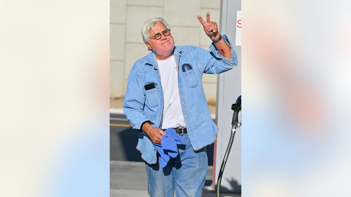 Jay Leno in a blue denim shirt and jeans and a white t-shirt underneath waves in Los Angeles after his accident