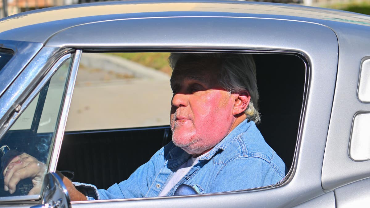 In a denim shirt, Jay Leno drives his car In Los Angeles after burn accident