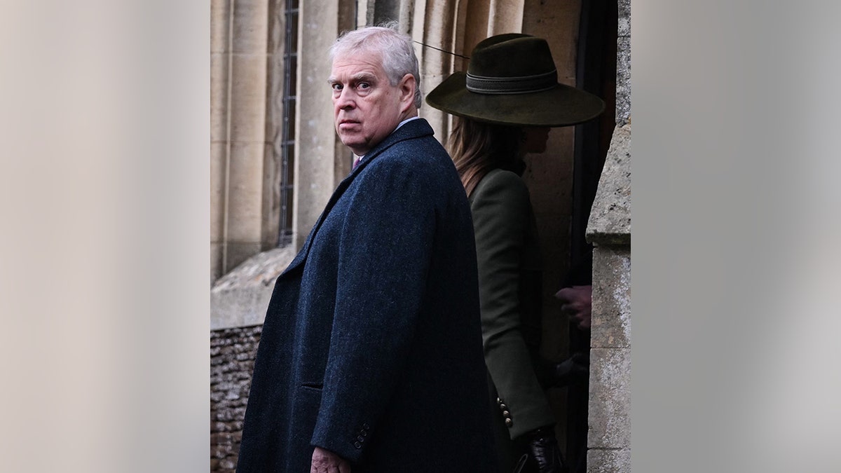 Prince Andrew looks directly back at the camera in a long coat while Kate Middleton walks inside in a green hat and coat