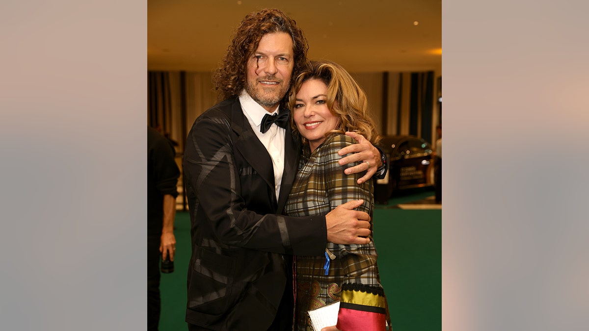 Frédéric Thiébaud in a patterned black suit jacket holds onto his wife Shania Twain in a green plaid jacket