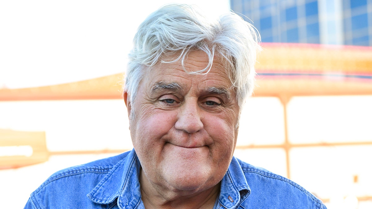 Jay Leno soft smiles wearing a denim blue long-sleeve shirt