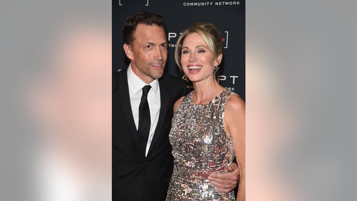 Andrew Shue in a black suit and black tie stands next to Amy Robuch in a sparkly gown