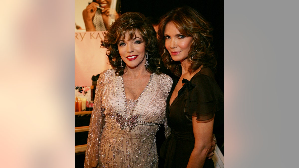 Joan Collins in a sparkly and jeweled gold dress poses for a photo with Jaclyn Smith in a black dress