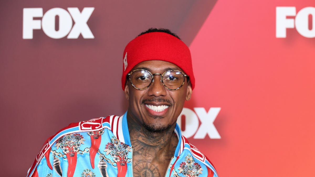 Nick Cannon smiles in a colorful turquoise shirt with red peppers on it
