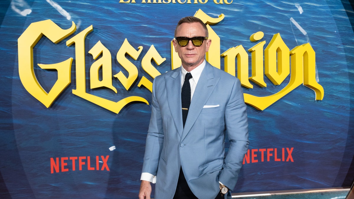 Daniel Craig on the red carpet for "Glass Onion: A Knives Out Mystery" in black sunglasses and a light blue suit with a black tie