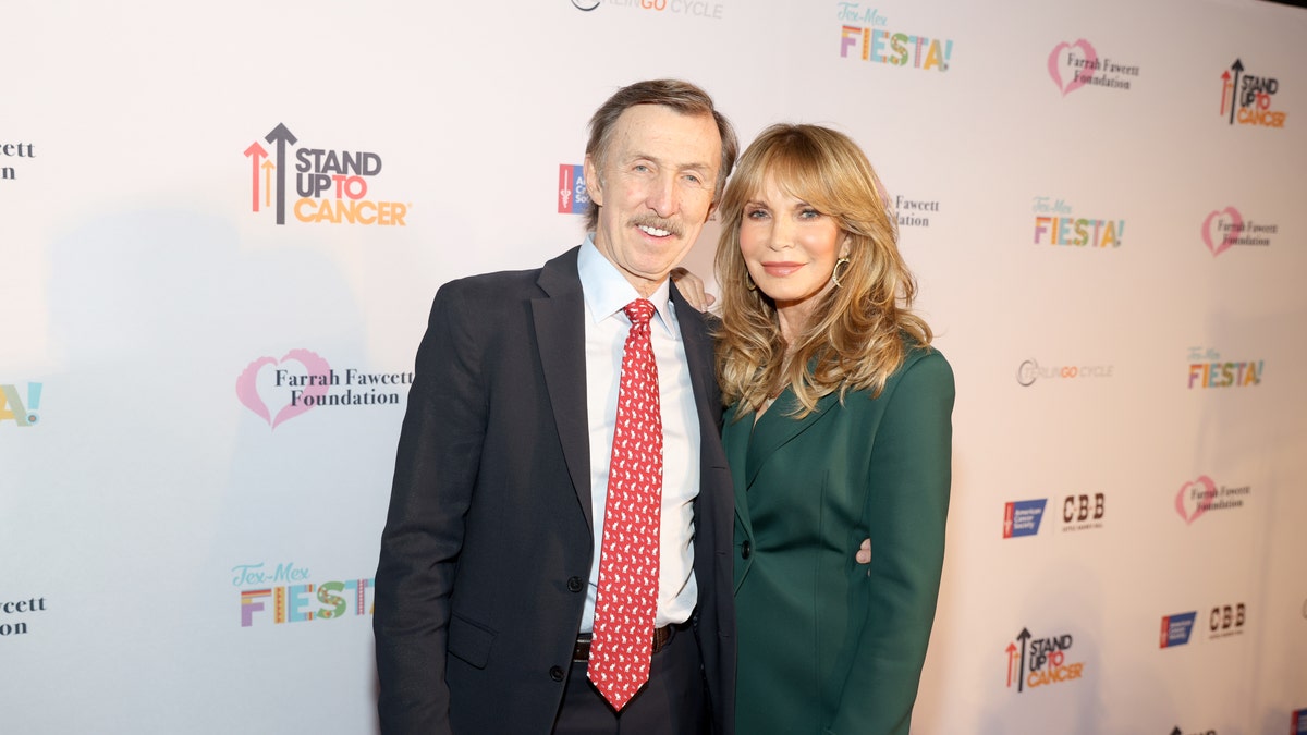 Dr. Brad Allen in a black suit and red tie poses with wife Jaclyn Smith in a green dress at the Farrah Fawcett Foundation Tex-Mex Fiesta Benefit