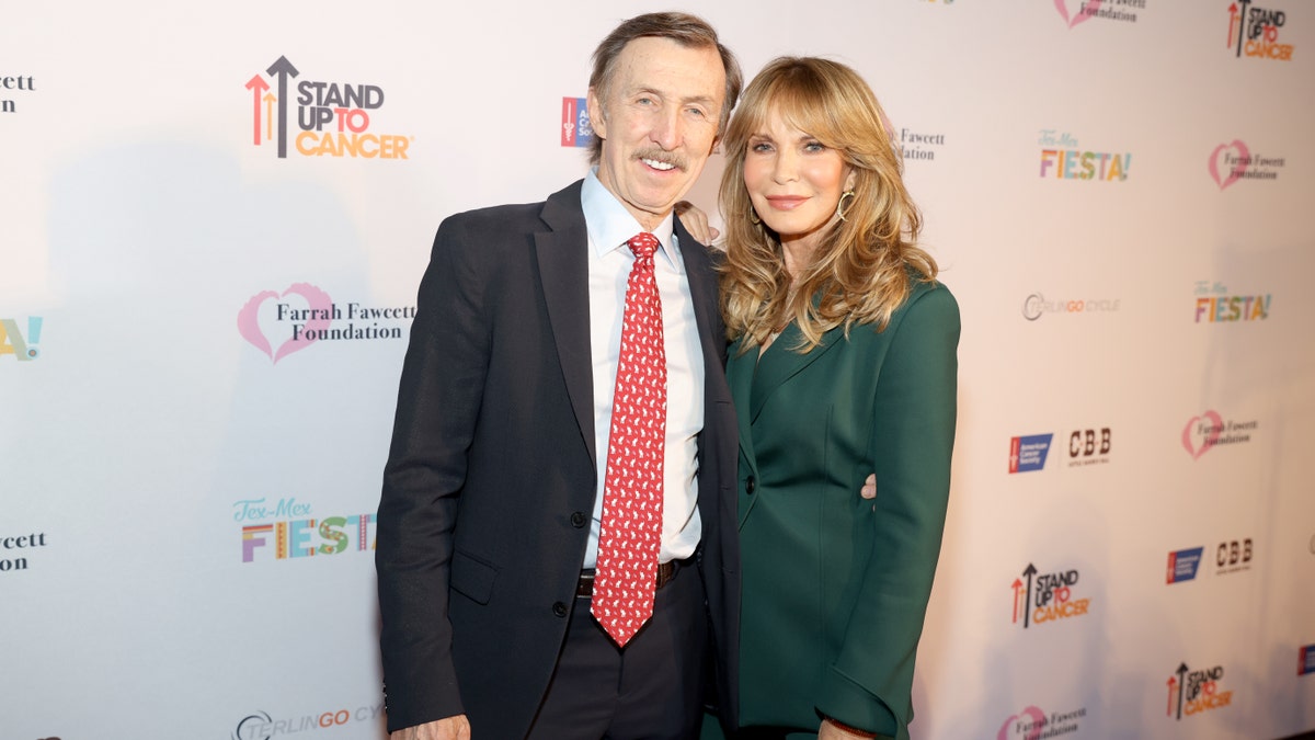 Dr. Brad Allen in a black suit and red tie poses with wife Jaclyn Smith in a green dress at the Farrah Fawcett Foundation Tex-Mex Fiesta Benefit