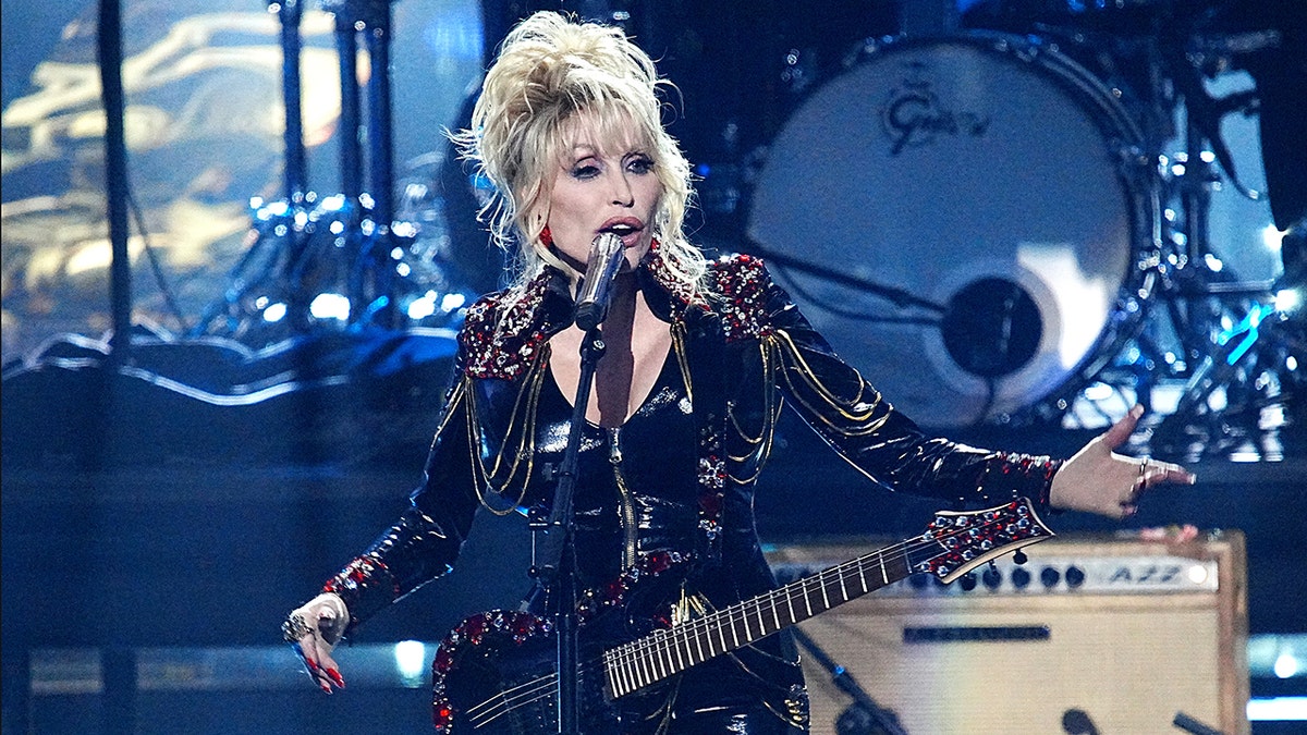Dolly Parton on stage with a guitar singing at the Rock & Roll Hall of Fame induction