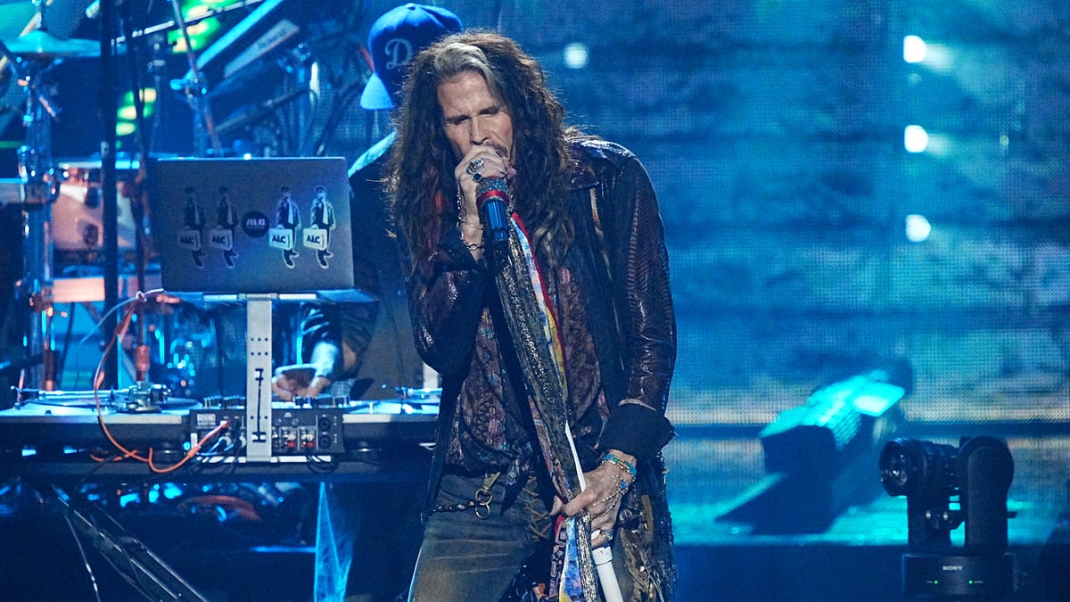 Steven Tyler in jeans and black leather jacket sings into the microphone