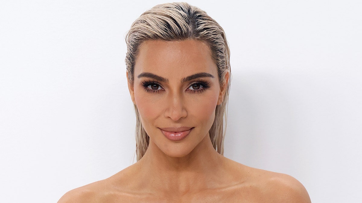 Kim Kardashian with a slicked back blonde hair-do smiles for a photo