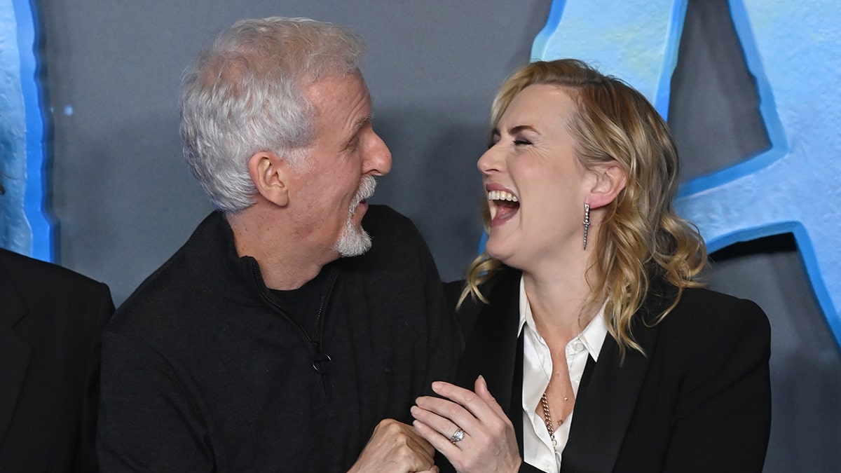 Kate Winslet holds on to James Cameron on the "Avatar' blue carpet as the two break out into a laugh