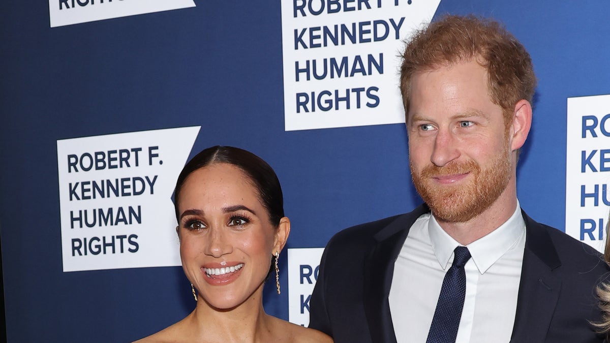 Meghan Markle in an off-the shoulder white gown and Prince Harry in a dark navy suit and tie on the red carpet