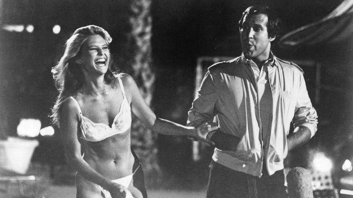 Chevy Chase puts hands in his pockets while filming with Christie Brinkley