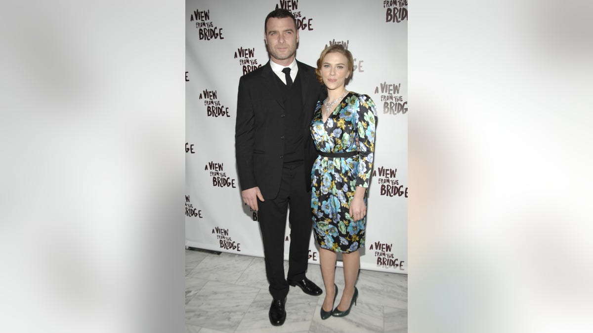 Lieve Schreiber in a black suit poses with Scarlett Johansson in a floral green and black and white shiny dress on opening night for their play in New York