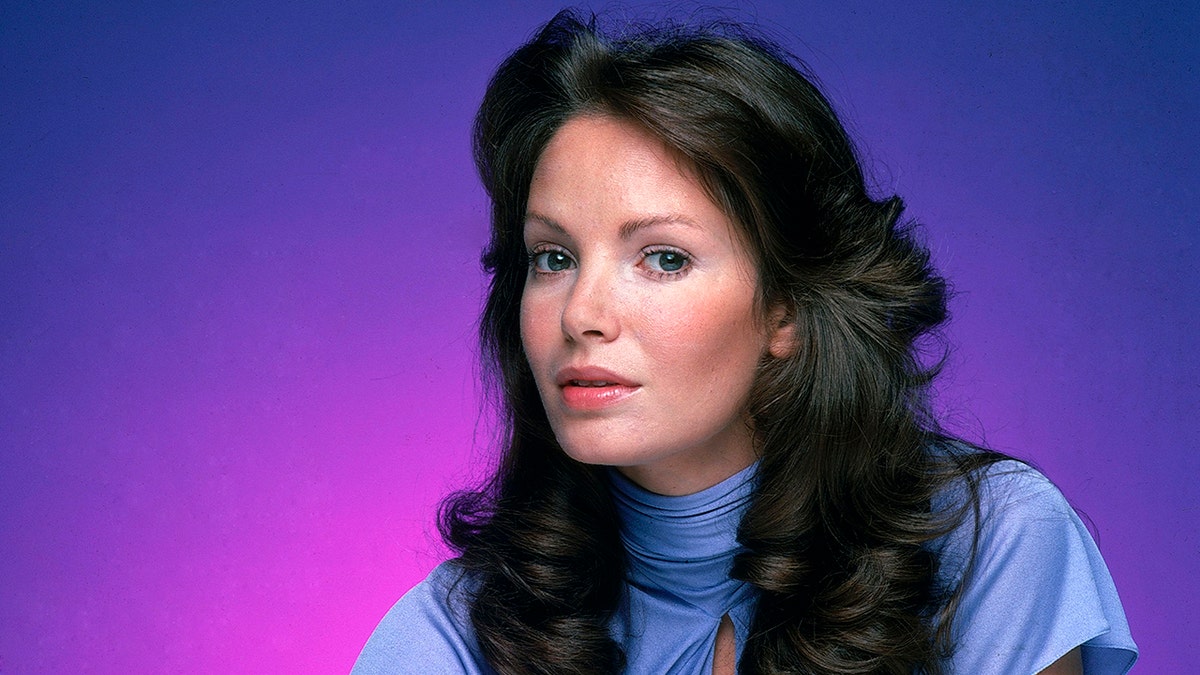 Jaclyn Smith in a light blue top with 70's hair and a ombre purple background for "Charlie's Angels"