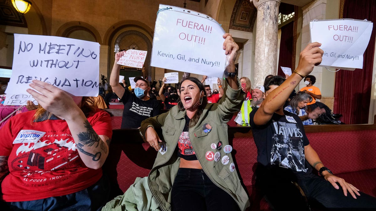 Protestors holding signs at an LA council meeting.