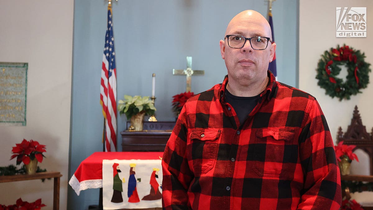 Reverend standing in a red and black checkered shirt inside the church