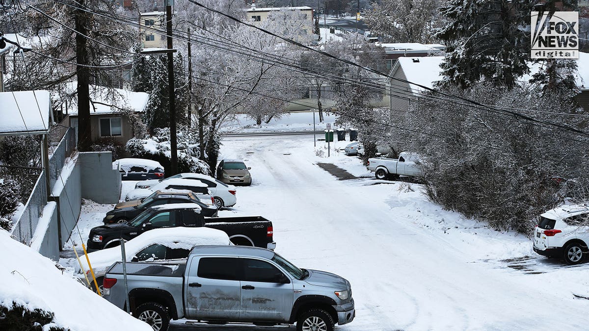A snow-packed road in a residential area with cars parked along the side of the road