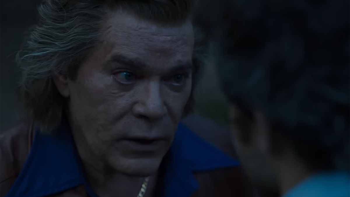Ray Liotta has a serious conversation with another character in the movie "Cocaine Bear," wearing a brown jacket and a blue collared shirt