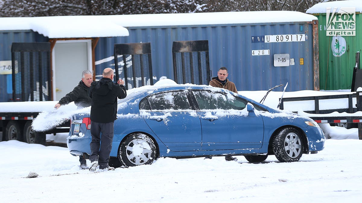 3 men brush snow off a car