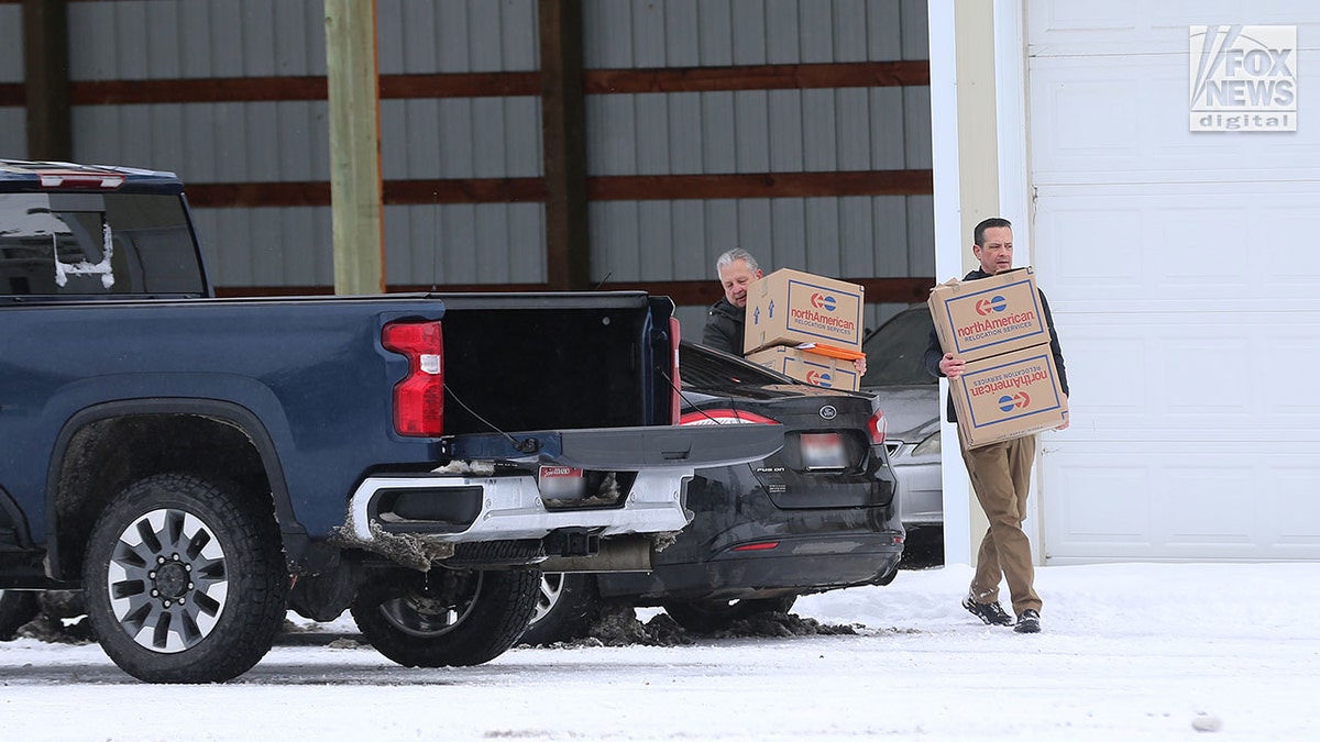 Two men carry boxes to a truck in the snow