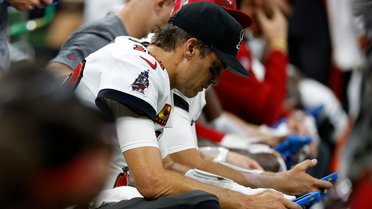 Tom Brady looks at a tablet on the sidelines