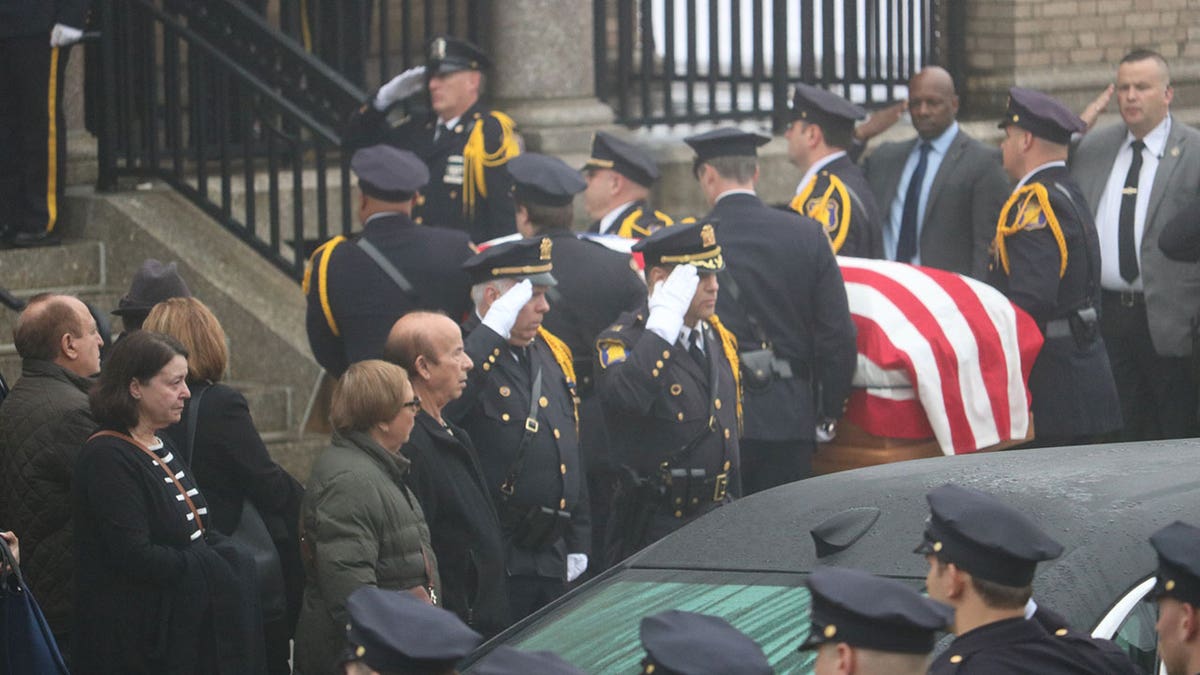 Two policemen wearing white gloves salute the flag-draped coffin