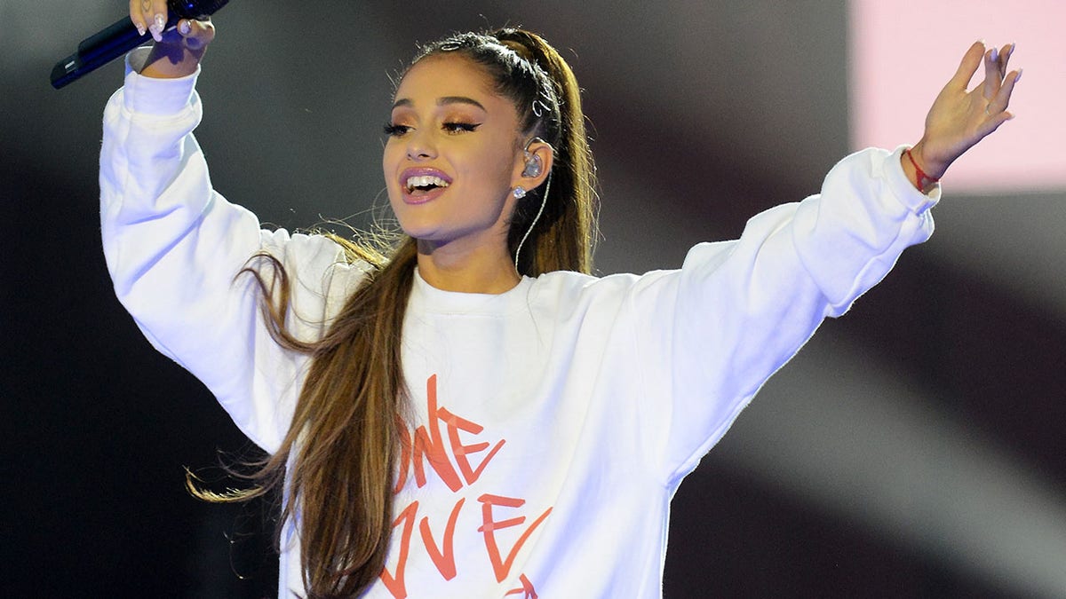 Ariana Grande sings on stage wearing an oversized white sweatshirt at concert