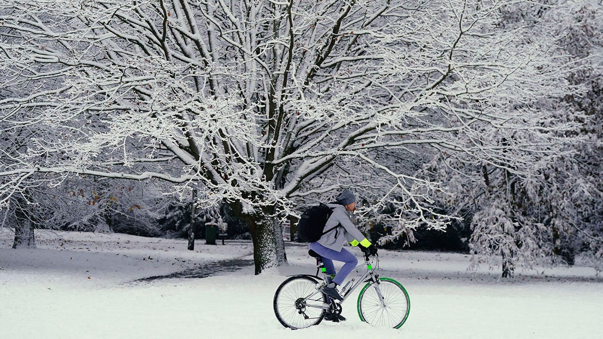 A man rides his bicycle through a snow-covered park in England