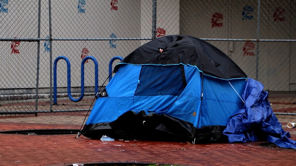 A homeless person makes holes in the top of their tent on a sidewalk in Portland on Dec. 8, 2022.