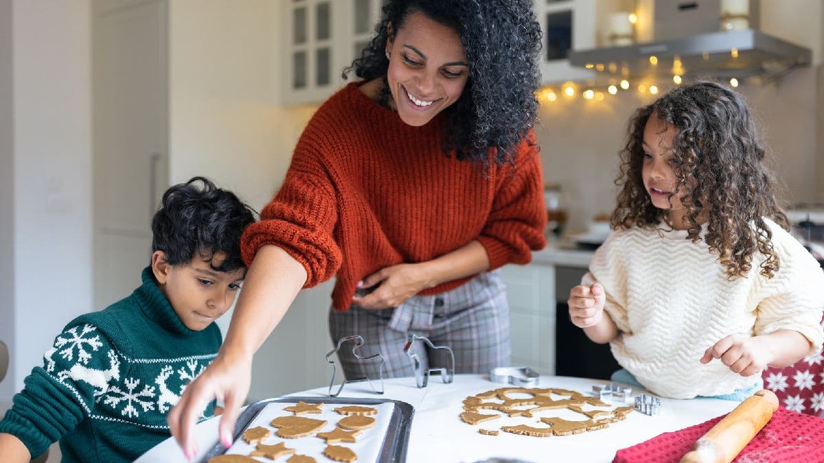 Woman arranges baked cookies on pan with children beside her