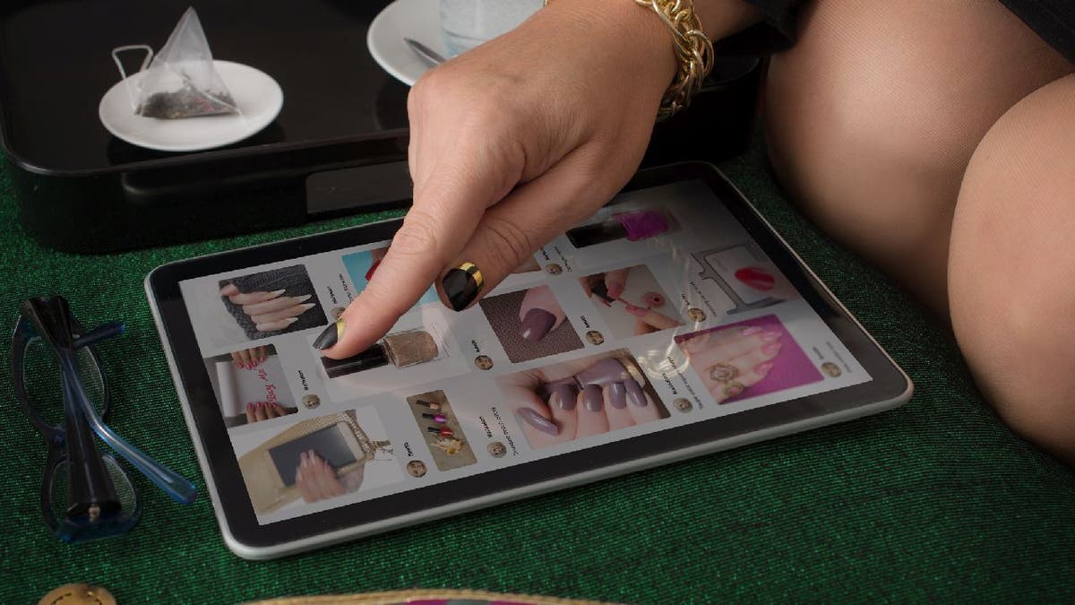 Woman looks at nail designs on website from tablet