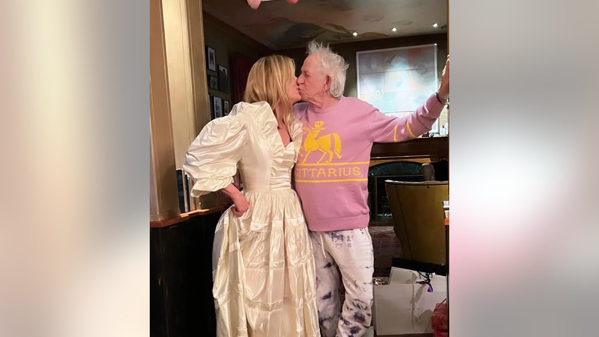 Keith Richards in a pink sweater kisses wife Patti Hansen in her wedding dress