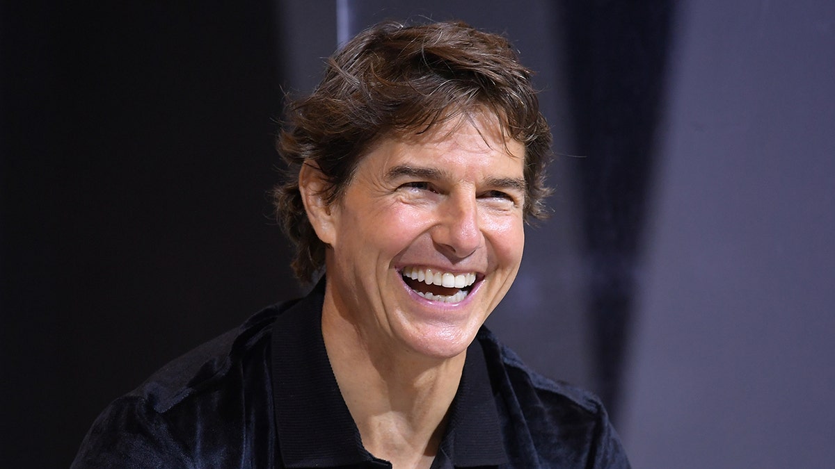 Tom Cruise smiles on stage while wearing a black polo shirt. 