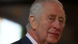 King Charles III looks off to his right in a pin-stripe navy blue suit