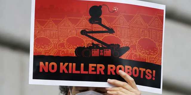 A woman holds up a sign while taking part in a demonstration about the use of robots by the San Francisco Police Department outside of City Hall in San Francisco, Monday, Dec. 5, 2022.