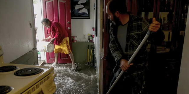 Hugo Archila, wearing red, and Jesus Armando Arredondo use a buckets and brooms to clear out water from Archila's home in Seattle's South Park neighborhood Tuesday morning, Dec. 27, 2022.