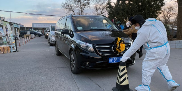 A worker in a protective suit removes a cone in front of a hearse outside a funeral home amid the COVID-19 outbreak in Beijing, China, Dec. 17, 2022.